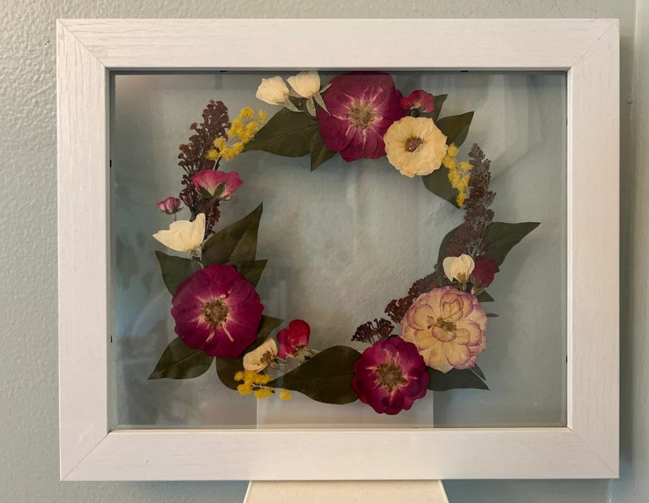 Framed floral wreath with pressed flowers on a gray wall